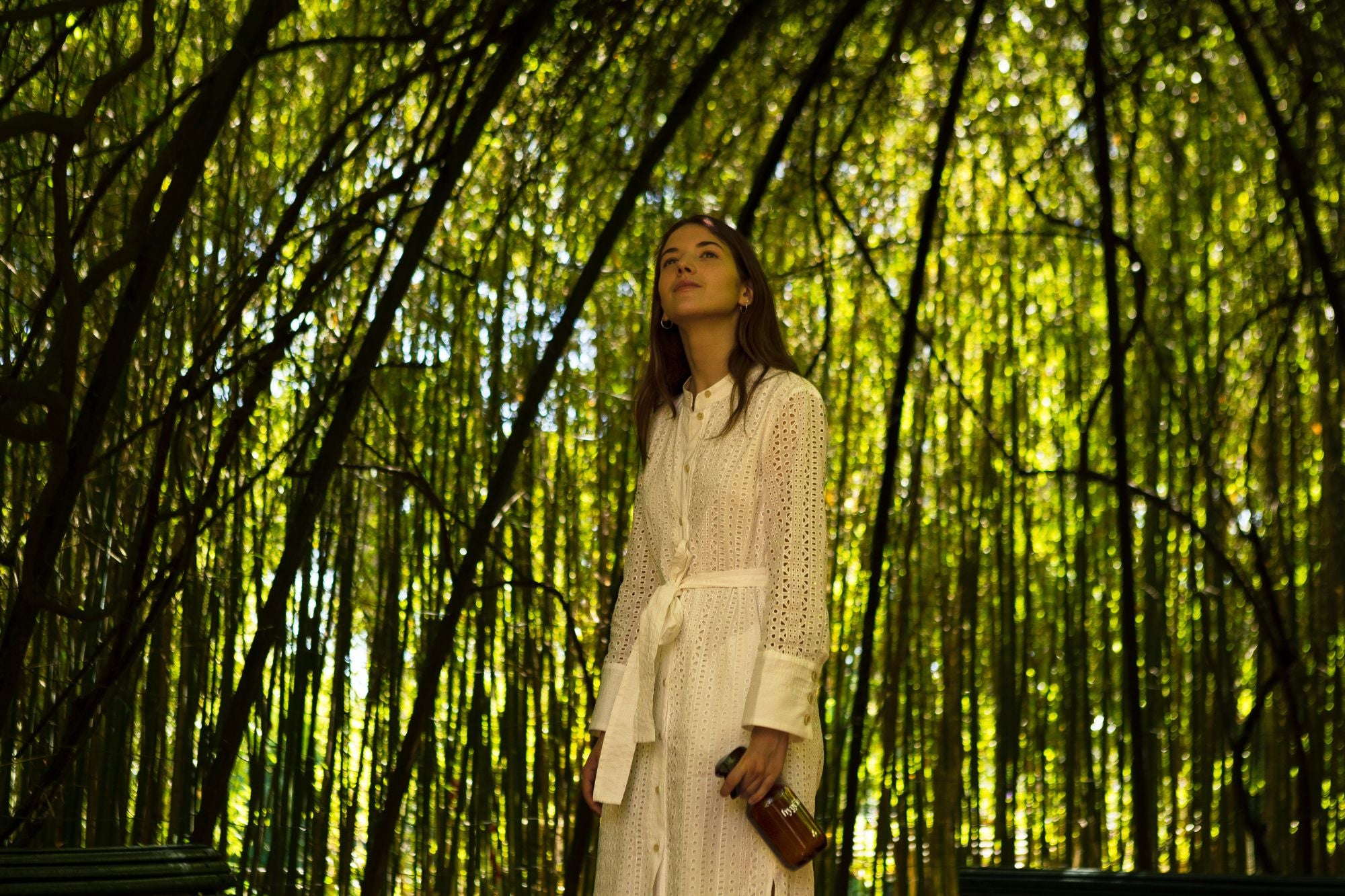 girl holding a spray bottle outside in nature underneath shade created by bamboo trees